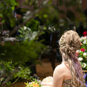 緑あふれる会場装花越しの新郎新婦様。おしゃれなウエディングヘアが印象的な一枚。|クオーリ クオーリ   〈エルフラットグループ〉の写真(22834336)