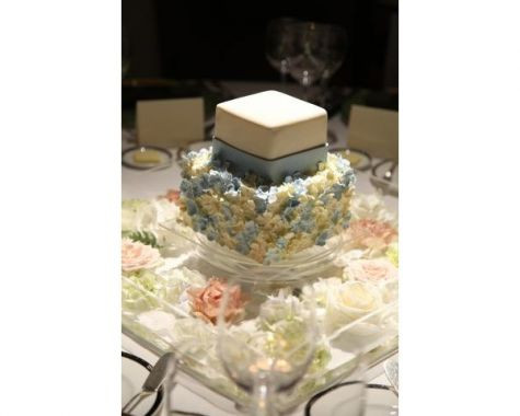 「幸せの青」サムシングブルーとアイボリーの清楚な配色がかわいらしい2段のスクエアタイプのウエディングケーキです。フリル状の小花がびっしりと敷き詰められた下段のケーキの上にシンプルなツートンカラーのケーキが乗せられています。クラシカルながらも個性的なデザインが光ります。