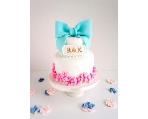 白のベースに大きなリボンが乗せられた、2段タイプのウエディングケーキです。シュガークラフトの大きなリボンと小花がかわいらしいカジュアルさを演出。ポップなブルーとピンクの配色が、鮮やかでガーリーな印象です。新郎新婦のイニシャルとプレートが映えるデザインのケーキです。